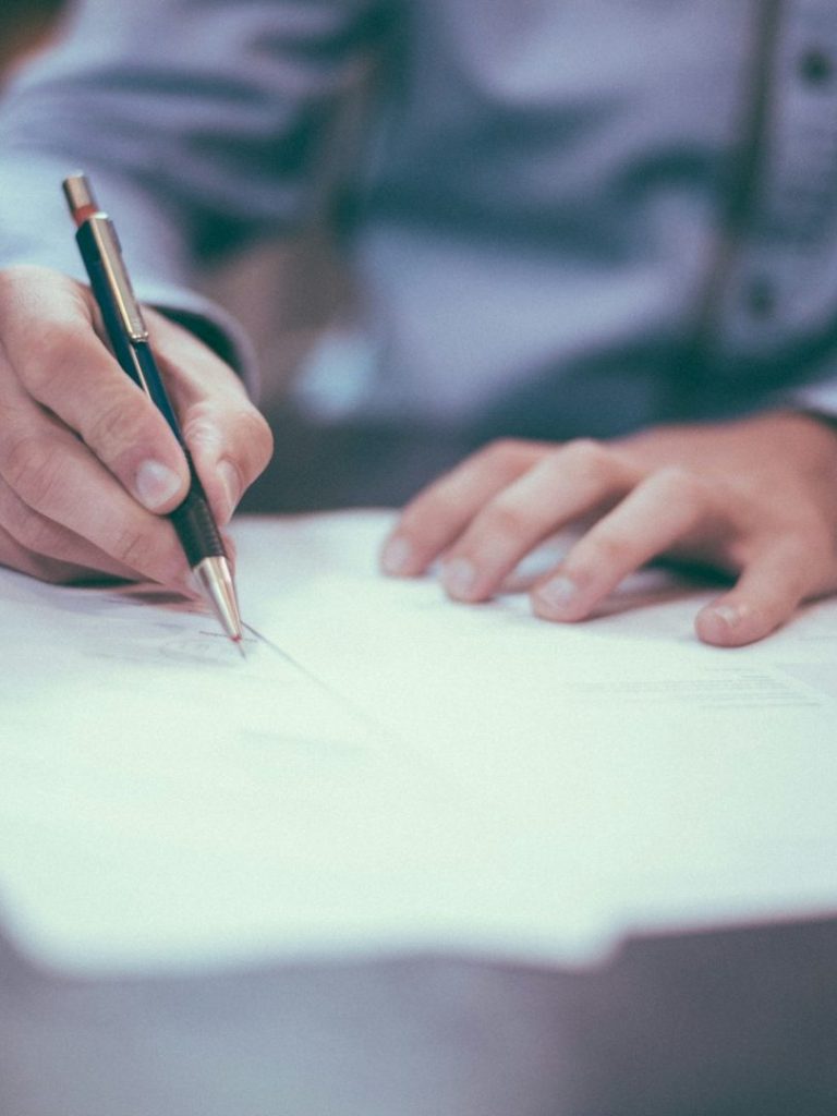 A hand writing on paper with a pen, resting on a flat surface.