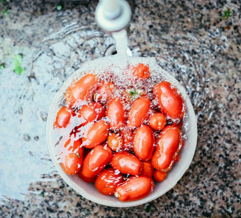 Fresh cherry tomatoes in a bowl under running water.