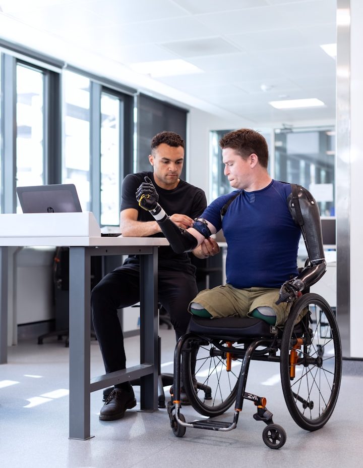 A person in a wheelchair is interacting with a professional about a prosthetic arm.